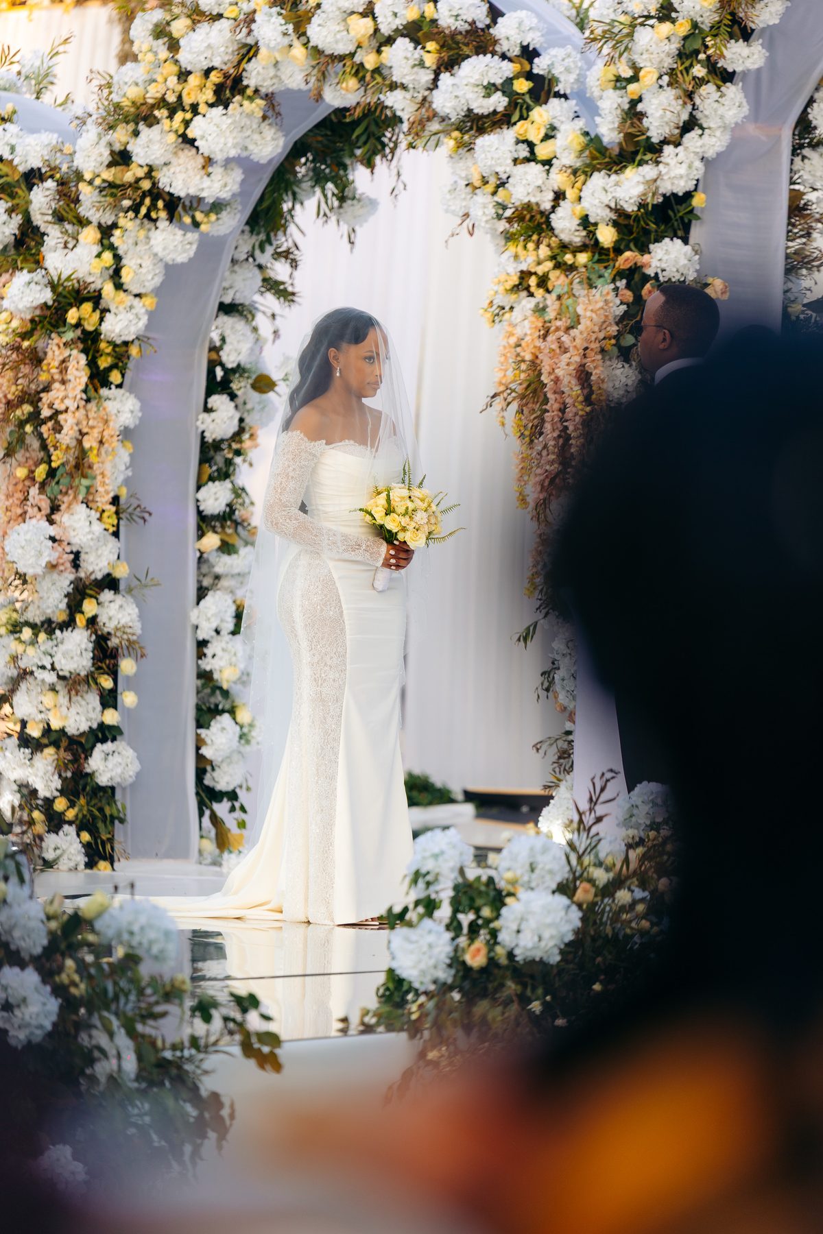 Ali & Dr. Lucy wedding in Tanga, Tanzania, by Kevins Events — the bride beneath the floral arch