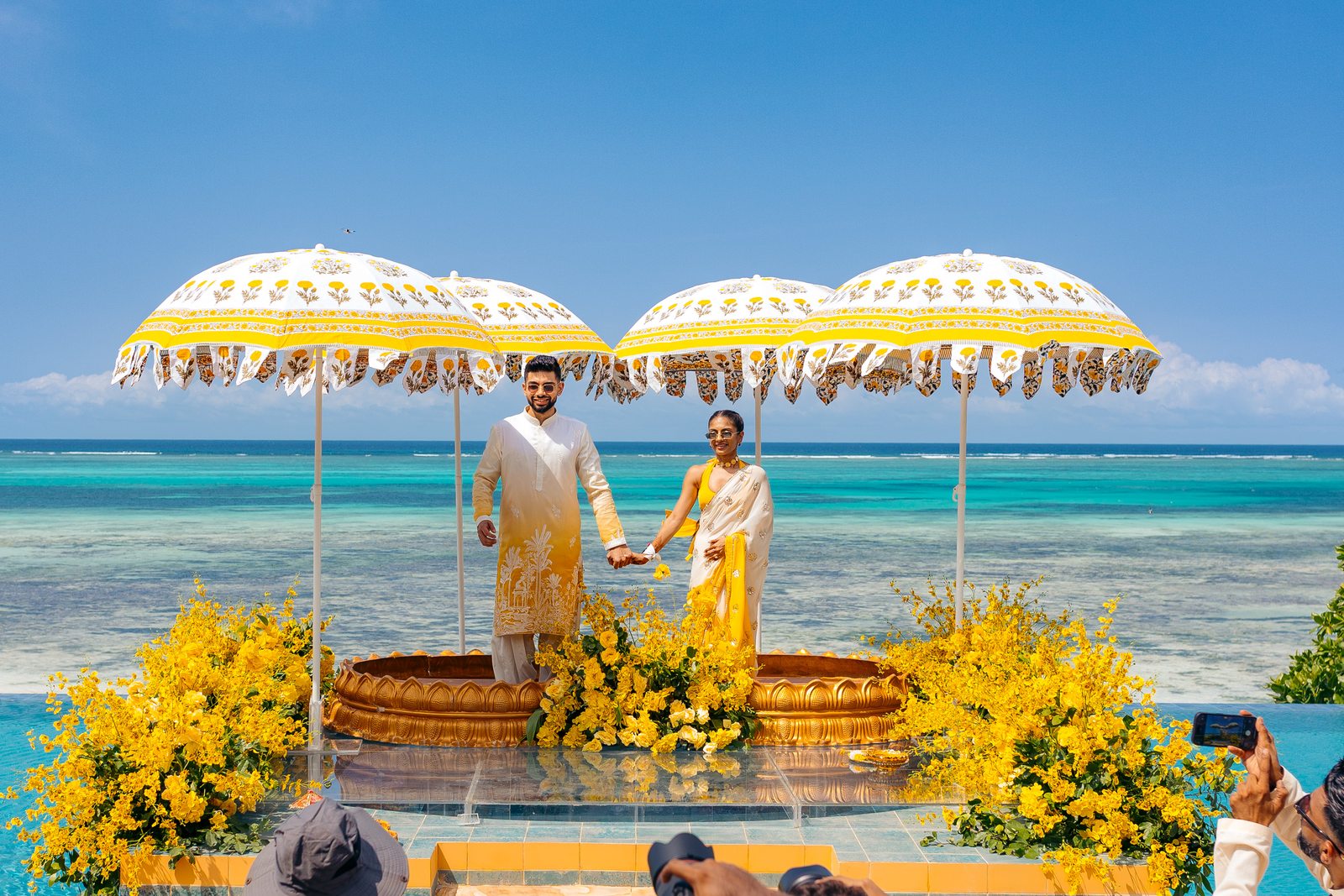 Sonia & Miraj wedding in Zanzibar — the couple by the Zanzibar sea beneath marigold parasols — by Kevins Events